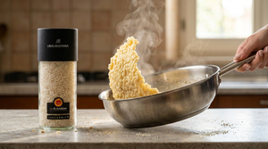 Vasetto di riso Sant’Andrea DOP accanto a una padella con risotto cremoso sollevata dal manico da una sola mano